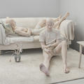 Two young men lounge on and in front of a couch on a rug in this jesmonite life-size sculpture by Daphne Wright