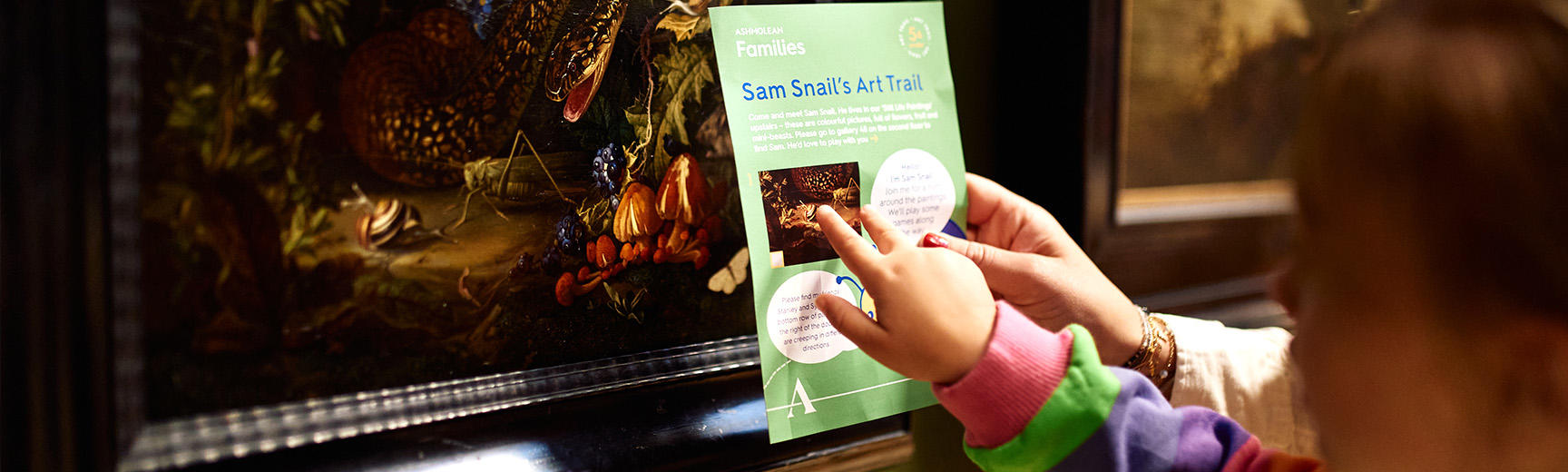 Children pointing at a painting in the galleries with a Snail trail leaflet 