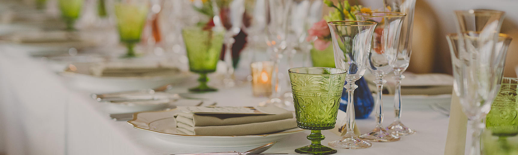 Image of a table laid for a wedding reception with green glasses, and spring flowers