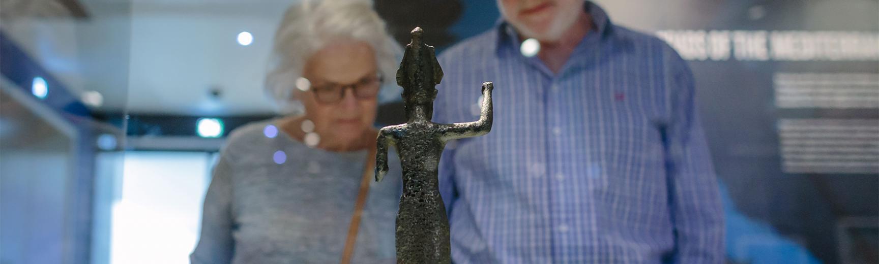 Two visitors look at a metal figurine that's inside a glass museum case