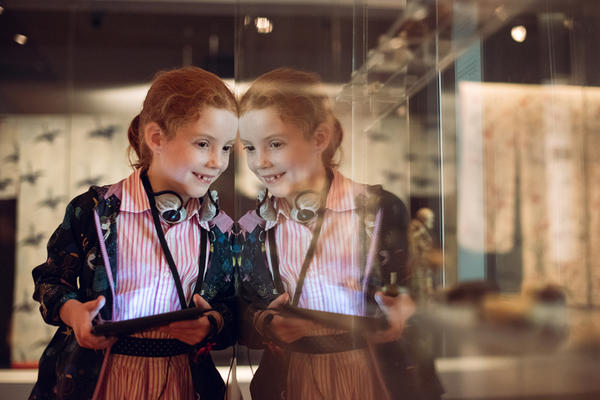 A smiling girl holds a multimedia guide and looks into a glass museum case
