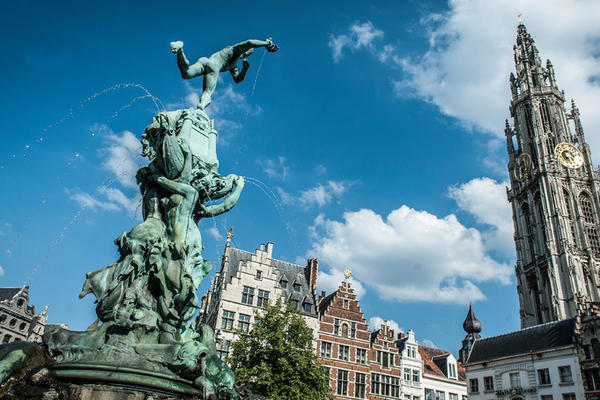 A photograph of the top of a fountain and Cathedral of our Lady in Antwerp against a bright blue sky