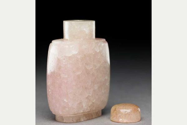 Small bottle for carrying snuff, made from rose quartz. A lid sits alongside the bottle in the image.