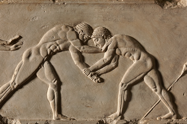 Stone relief of two men wrestling, with athletes either side
