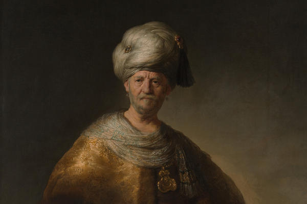 A painting of a white man in oriental dress consisting of a yellow cape and white turban, the background is plain, by Rembrandt.