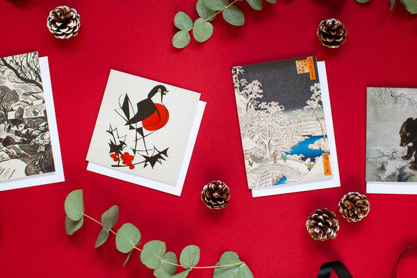 Four Christmas Cards against a red background, surrounded by pine cones and green foliage