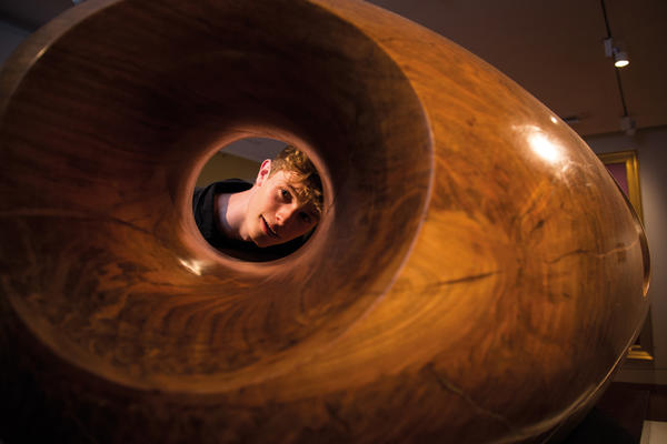 A man looks through the hole in the centre of a large wooden sculpture by artist Barbara Hepworth
