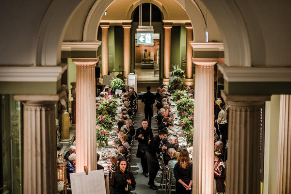 A view from high up of a gala dinner taking place in a long gallery at the Museum, with columns in the foreground