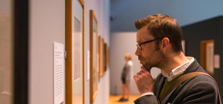A man takes a closer look at an artwork on display on a gallery wall