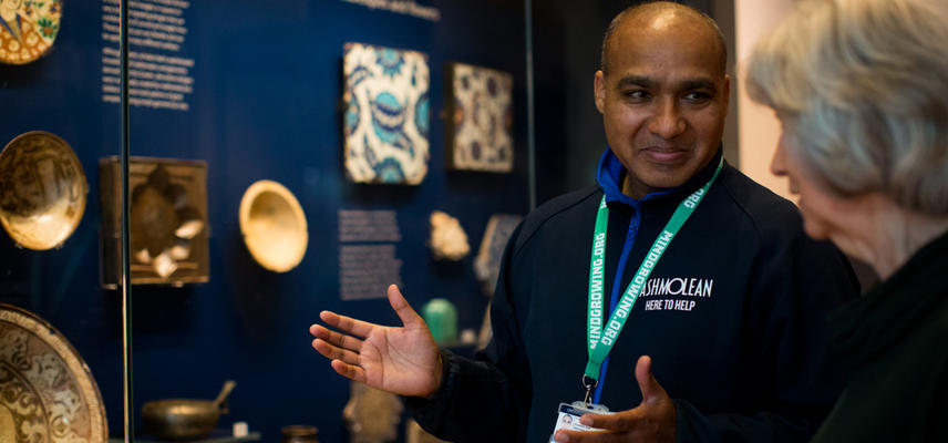 Museum staff member and volunteer stand in front of a case of museum objects on display