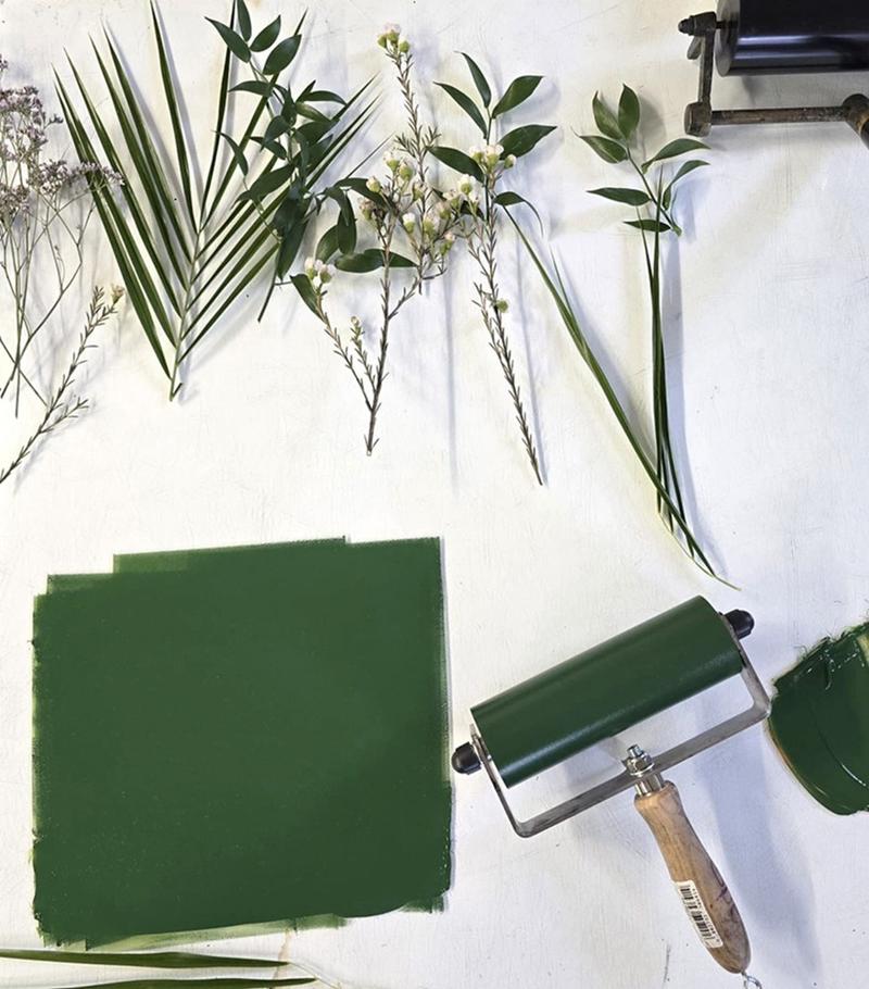 A paint roller with green paint and plant materials such as leaves and stems