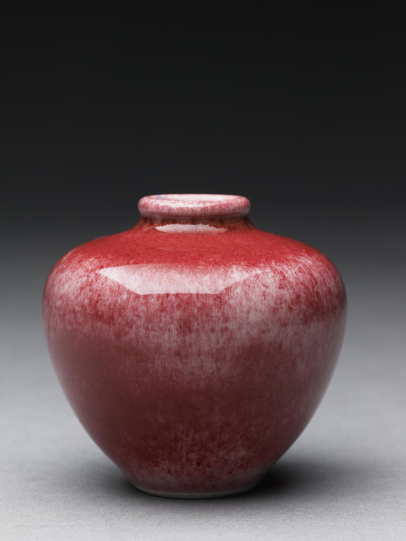 A small round Japanese vase with red glaze and a narrow spout
