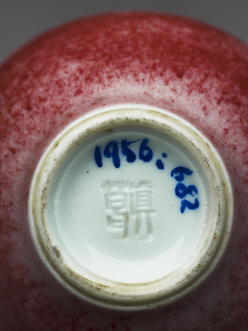 A close up image of the bottom of a red vase with a stamp from Kozan's workshop and an accession number in blue ink