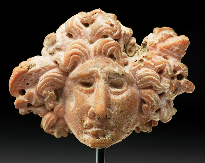 An ancient head of Medusa on a stand made out of red coral with serpent's hair billowing out of the staring face