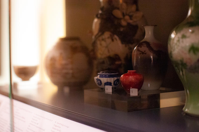 A dimly lit photo of Japanese vases in a case, with small red vase in central focus