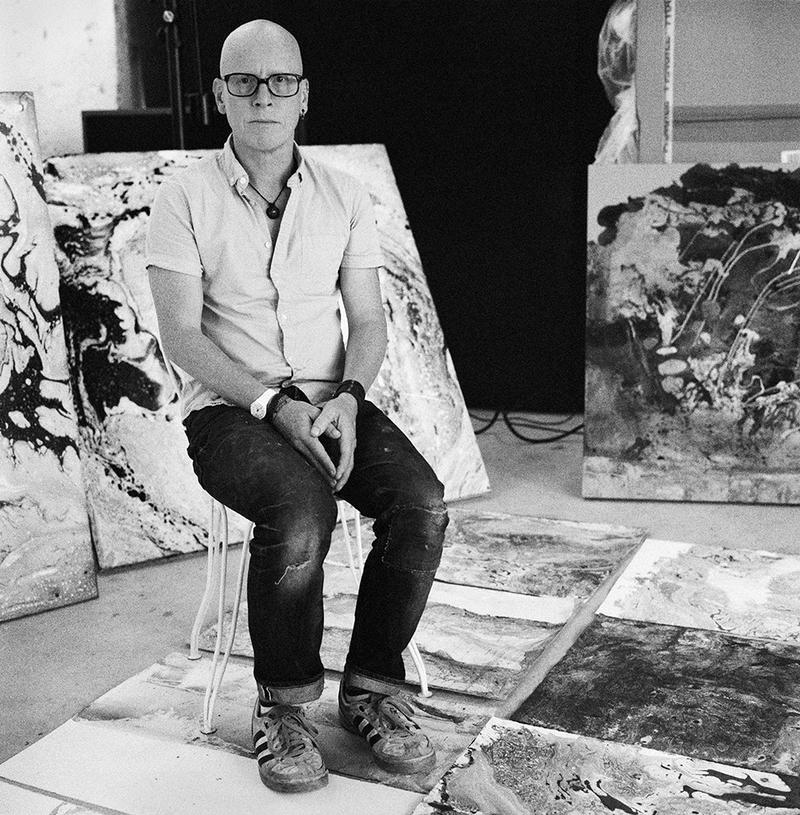 Black and white photo of Stanley Donwood in studio with artworks on the floor