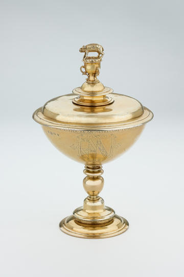 A gold-coloured cup and lid, with a small pig figure perched on the very top