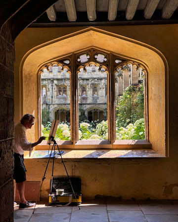 Francis Hamel painting with an easel inside one of the Oxford colleges looking out at the sun and shadows