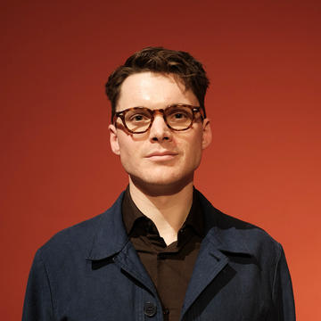 Peter Thompson's staff portrait against a red background
