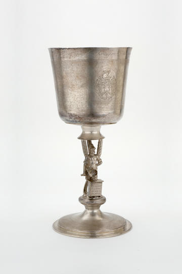 A tall silver goblet with decorated stem and a crest stamped on the cup