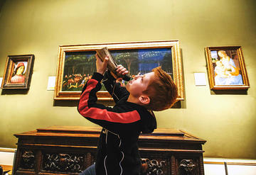Child playing a horn instrument in the galleries with paintings behind him