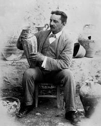 Black and white photograph of Sir Arthur Evans holding a rhyton from the Hall of the Double Axes of the Palace of Minos at Knossos dated 1901